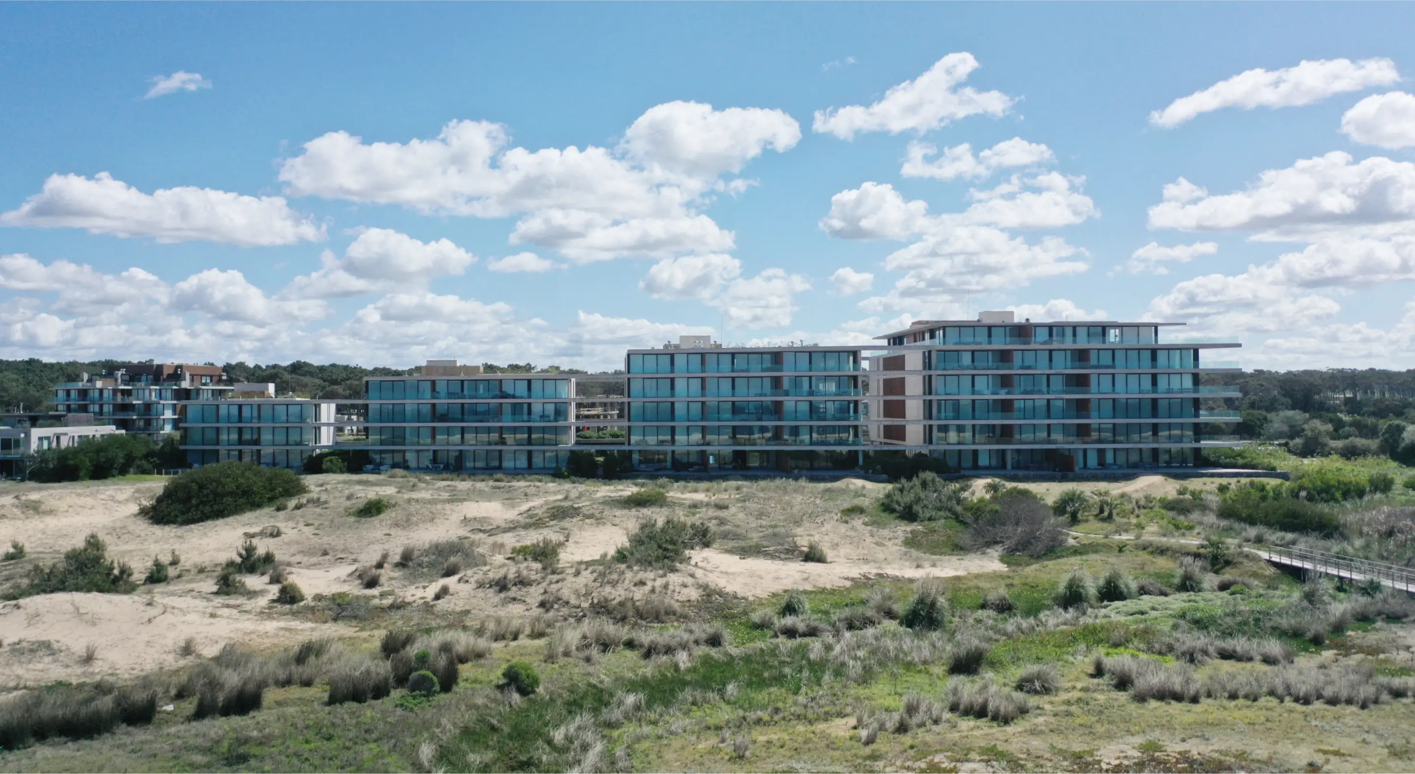 Impresionante vista de un moderno complejo residencial situado en primera línea de playa, destacando su arquitectura vanguardista y amplios ventanales con vistas panorámicas al mar.