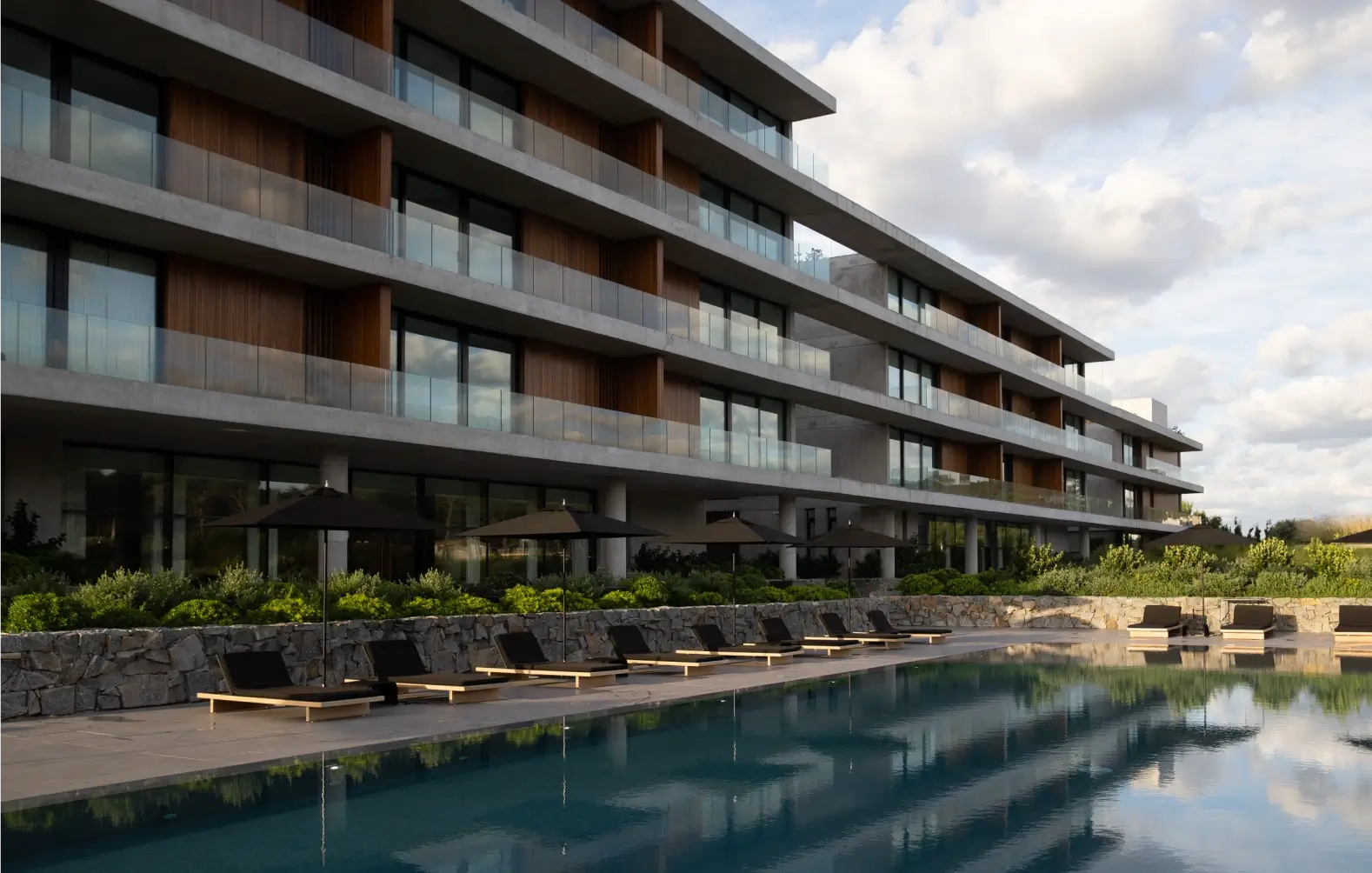 El equilibrio perfecto entre naturaleza y diseño moderno Edificio moderno con piscina al aire libre. El edificio, de varios pisos, cuenta con balcones privados y grandes ventanales. La piscina está rodeada de tumbonas y sombrillas, y se encuentra en un entorno natural con vegetación.