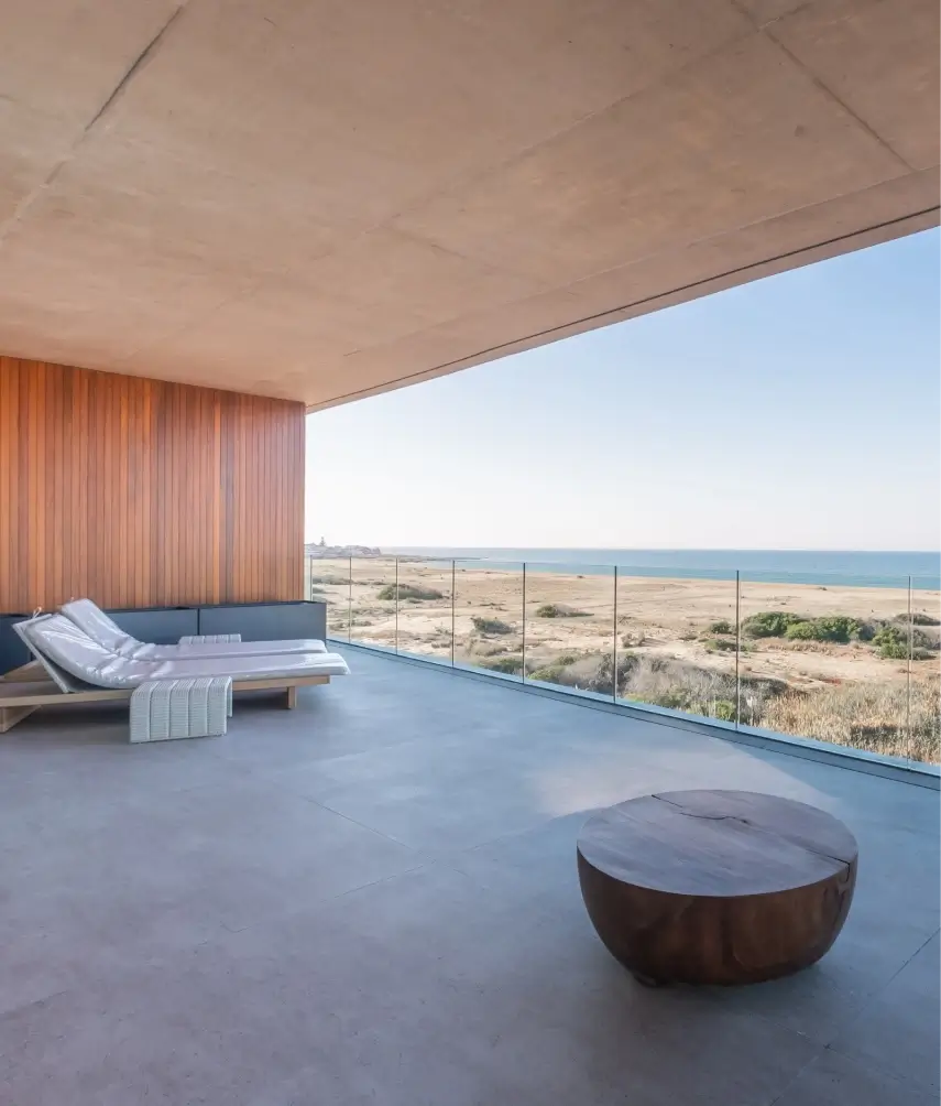 El lujo de vivir frente al mar: Terraza con vistas panorámicas Amplia terraza con vistas panorámicas al mar. La terraza cuenta con mobiliario de exterior moderno, incluyendo tumbonas y una mesa de centro de madera. El piso es de baldosas de gran formato y la pared lateral está revestida en madera.